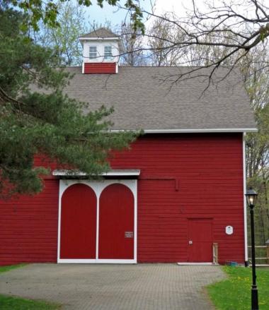 A red barn house with french doors and white trim and a white lookout on top of the roof. 