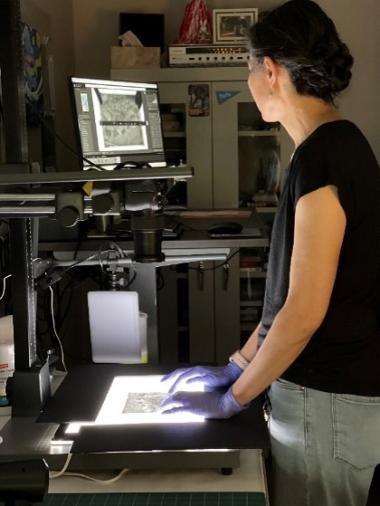 A woman scans records on a light box while looking at it transmitted onto the computer. 