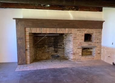 18th century brick fireplace with a behive oven and dark wooden mantle around the fireplace. 